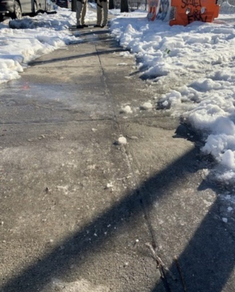 Partly cleared New York City sidewalk with snow banks and patches of ice